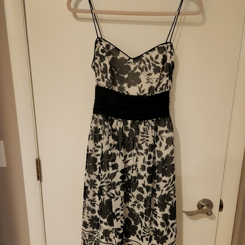 Woman's white and black floral, sleeveless strap dress with black waist sash.